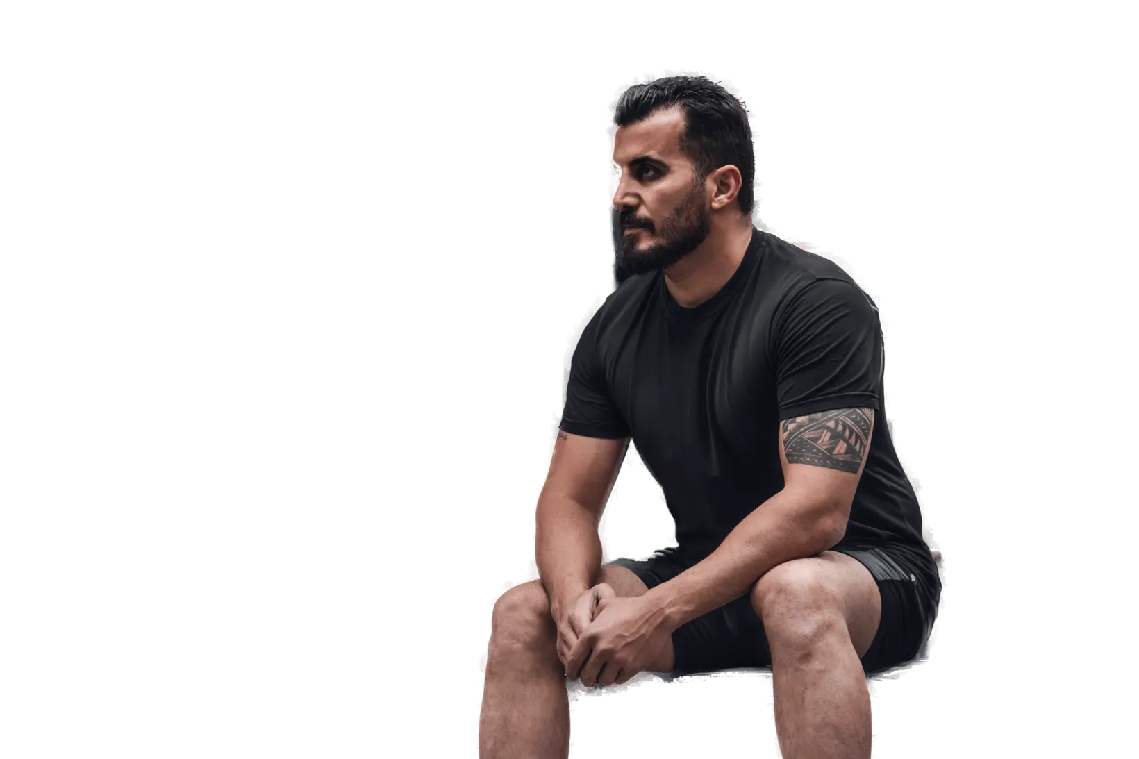 A man in his thirties sitting on a bench in a dark gym, looking ahead calm and focused